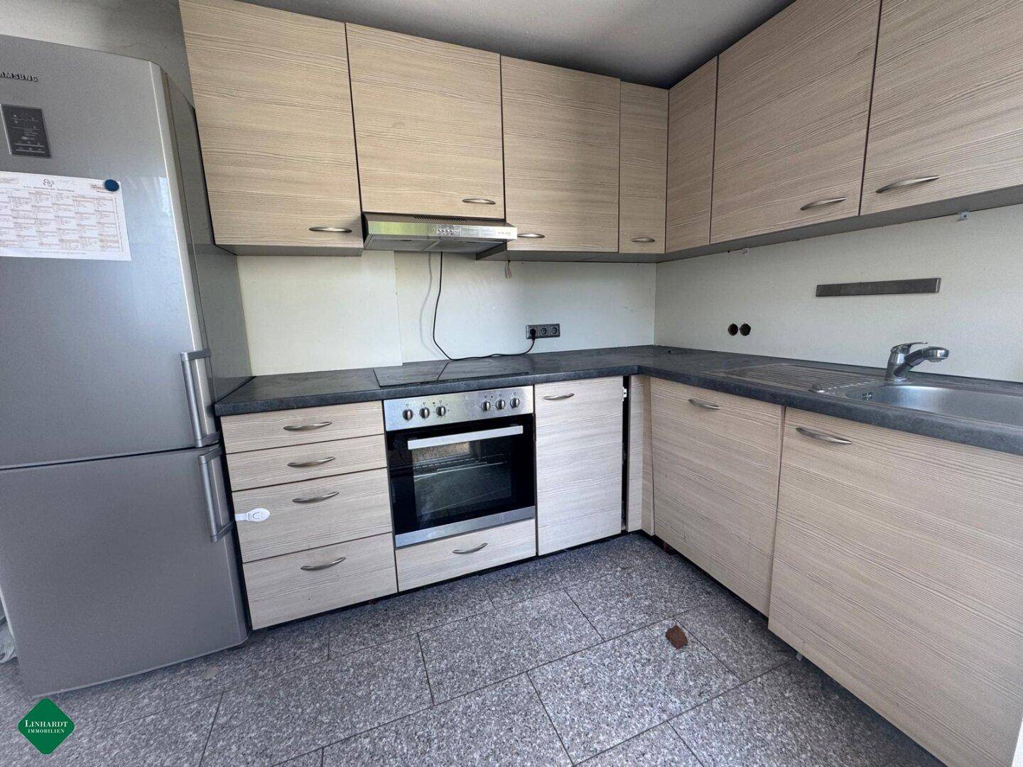 Einbauküche mit hellen Holzfronten, Herd, Kühlschrank und Spüle, mit grauem Fliesenboden.
