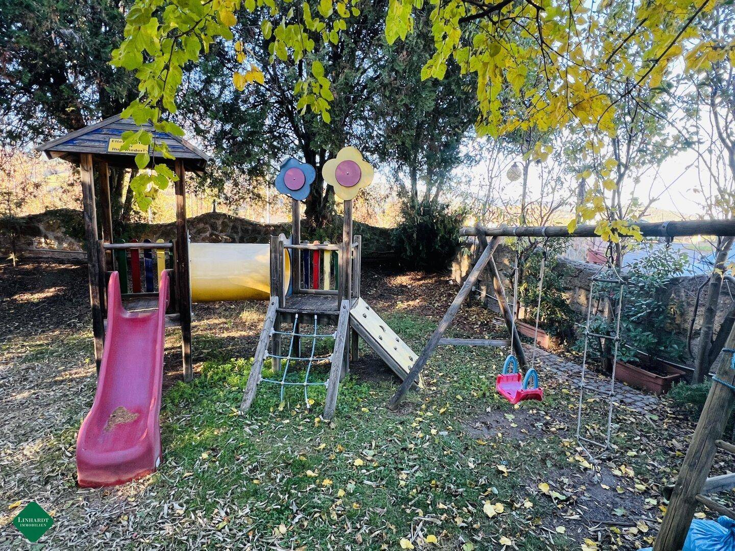 Ein kinderfreundlicher Spielplatz mit Rutsche, Schaukel und Klettergerüst, umgeben von Bäumen.