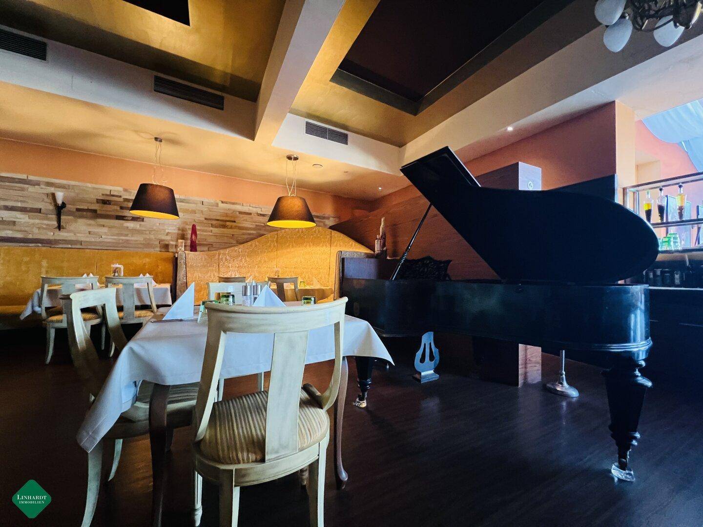 Ein eleganter Restaurantbereich mit gedeckten Tischen, dunklem Holzboden und einem Flügel als Blickfang.