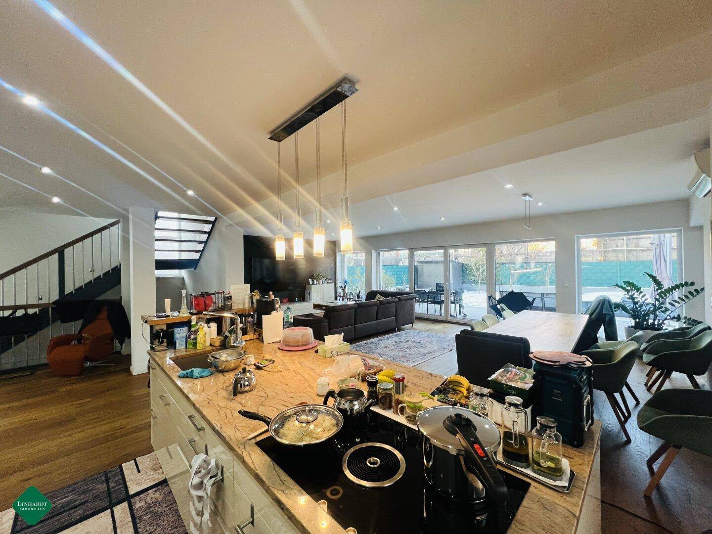 Moderne offene Küche mit Kochinsel und Essbereich, die in einen hellen Wohnbereich übergeht.