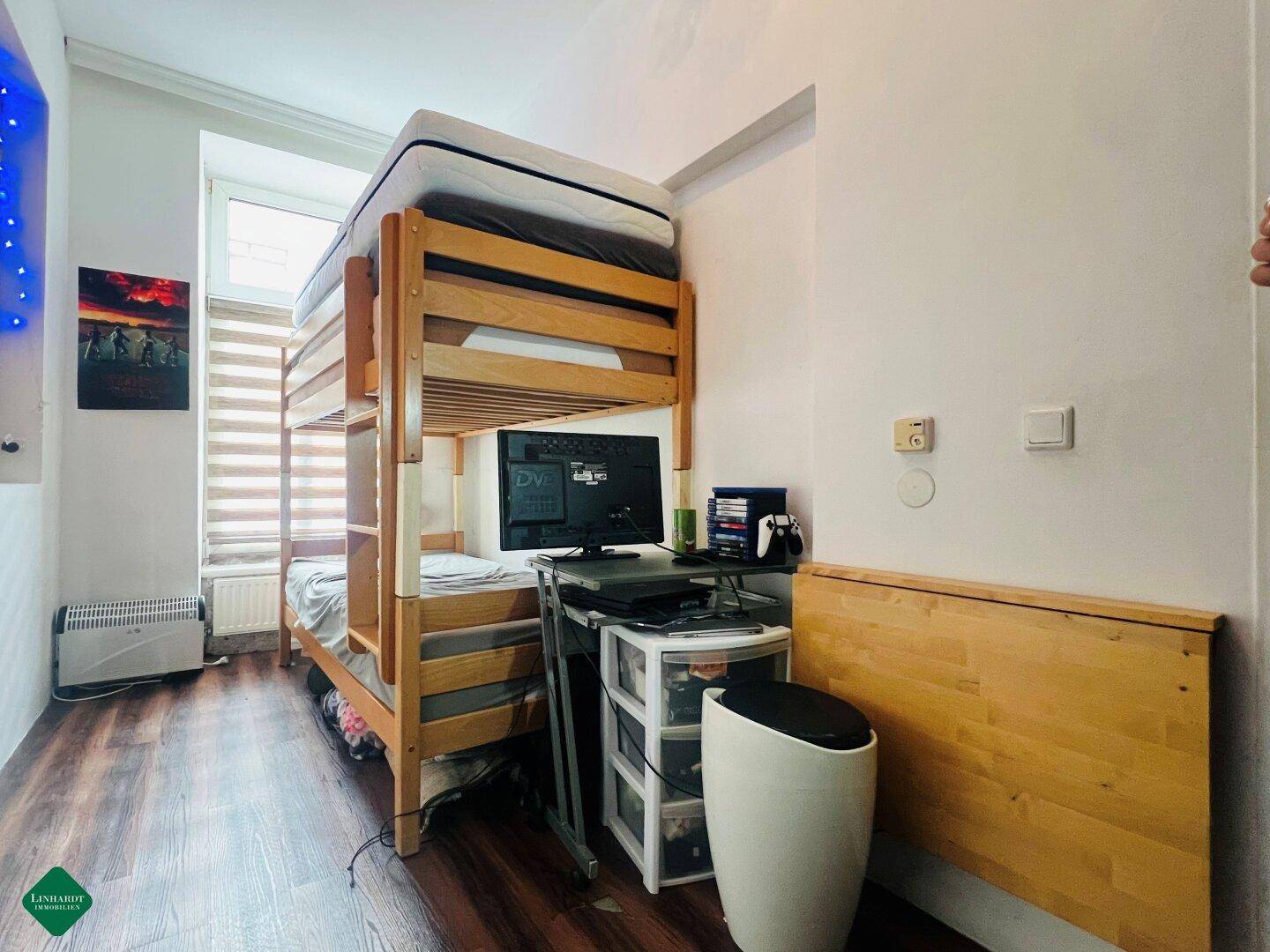 Kinderzimmer mit Etagenbett aus Holz, Schreibtisch und dunklem Laminatboden.