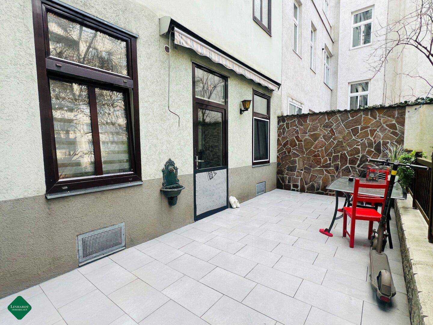 Gepflasterte Terrasse im Hinterhof mit Sitzgelegenheiten und Steinmauer.