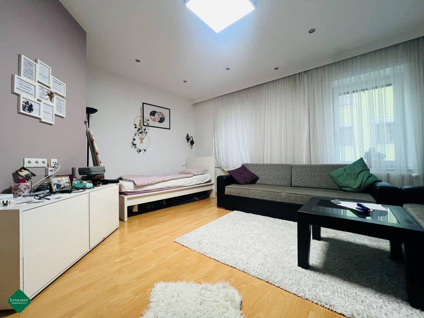 Helles Schlafzimmer mit Holzboden, einem Bett und einem Sofa, bietet vielseitige Nutzungsmöglichkeiten.