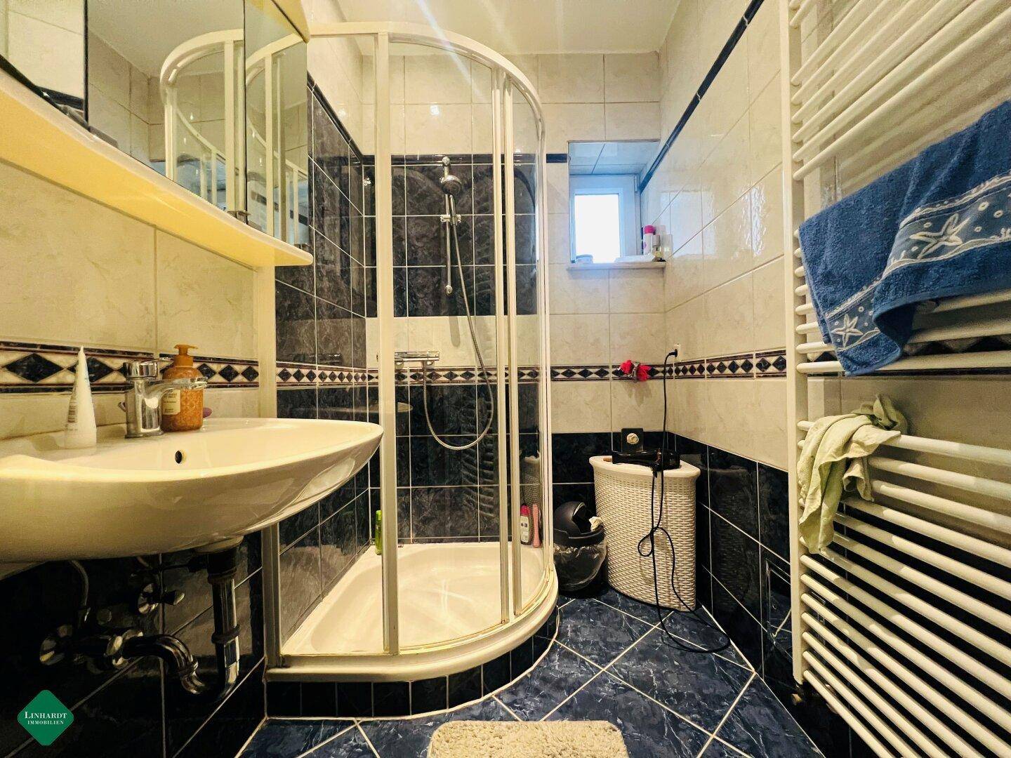 Badezimmer mit Eckdusche, Waschbecken, beheiztem Handtuchhalter und blauen sowie weißen Fliesen.