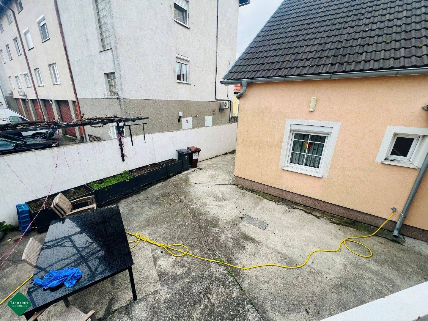 Gepflasterter Hinterhof mit Sitzgelegenheiten und Pflanzkübeln zwischen den Gebäuden.