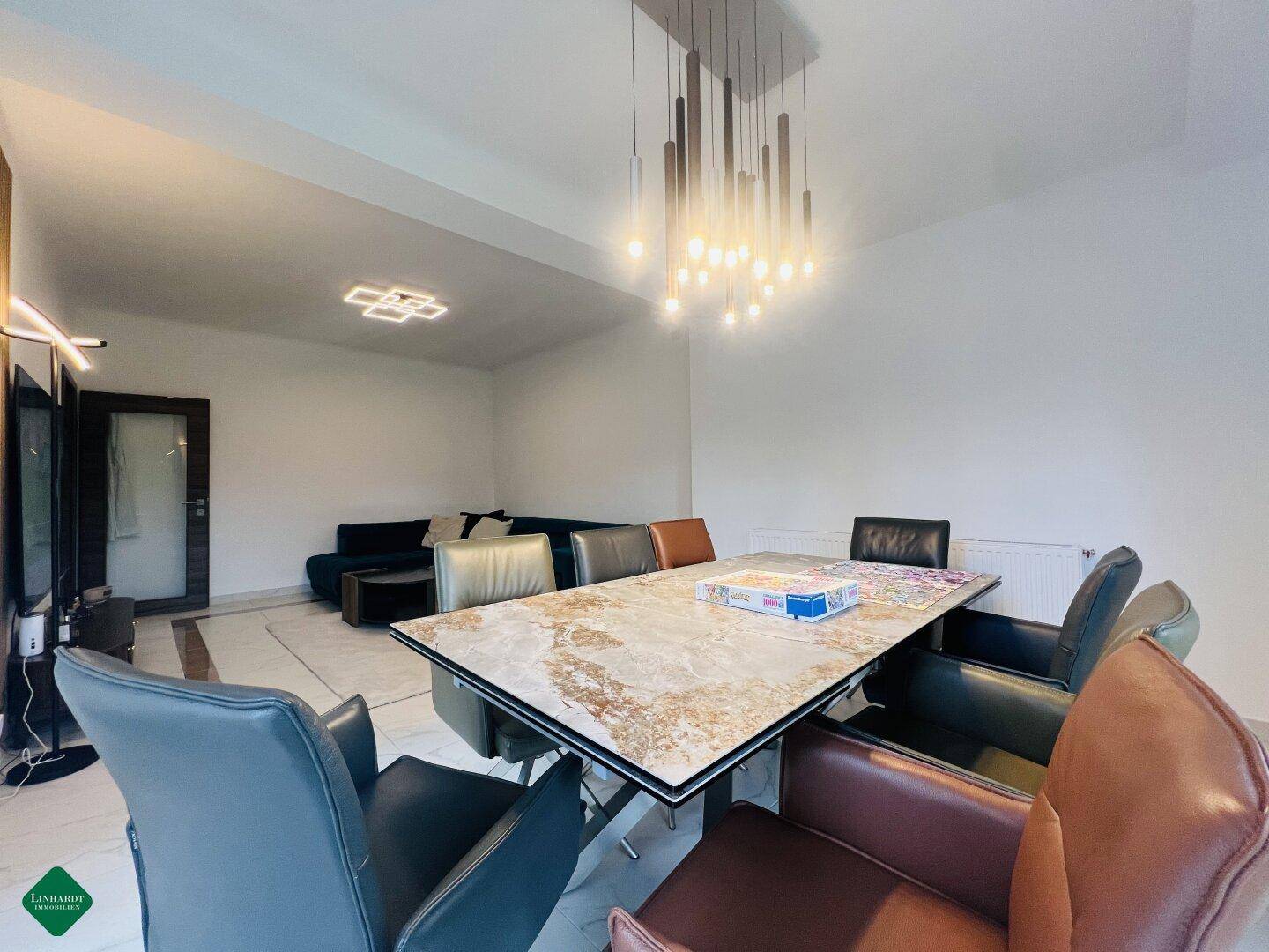 Eleganter Essbereich mit großem Tisch, verschiedenen Stühlen und moderner Hängelampe.