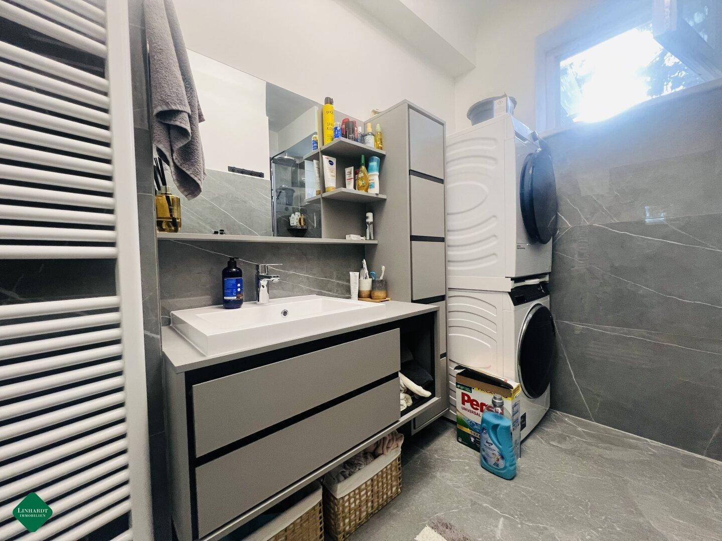 Modernes Badezimmer mit grauen Fliesen, Einzelwaschbecken und Waschmaschine/Trockner.