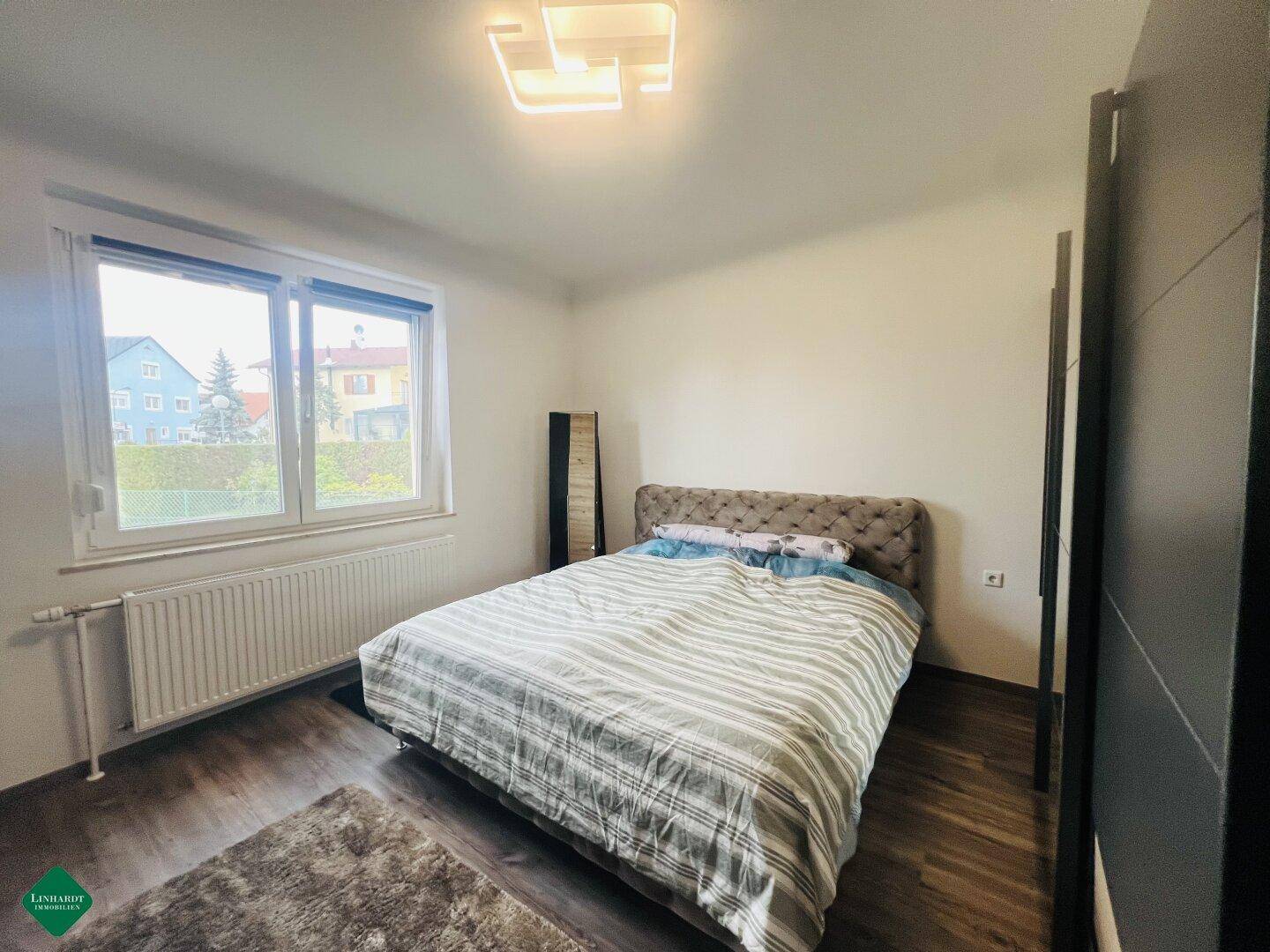 Helles Schlafzimmer mit Doppelbett, Holzfußboden und großem Fenster mit Blick ins Grüne.