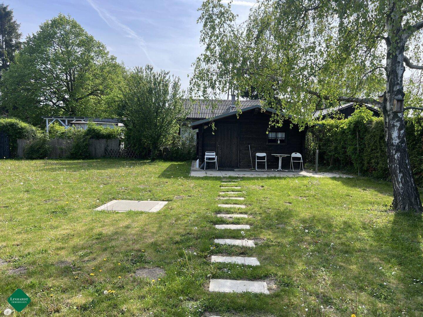 Kleines Holzhaus mit einfacher Terrasse und großem Rasenbereich in sonniger Umgebung.