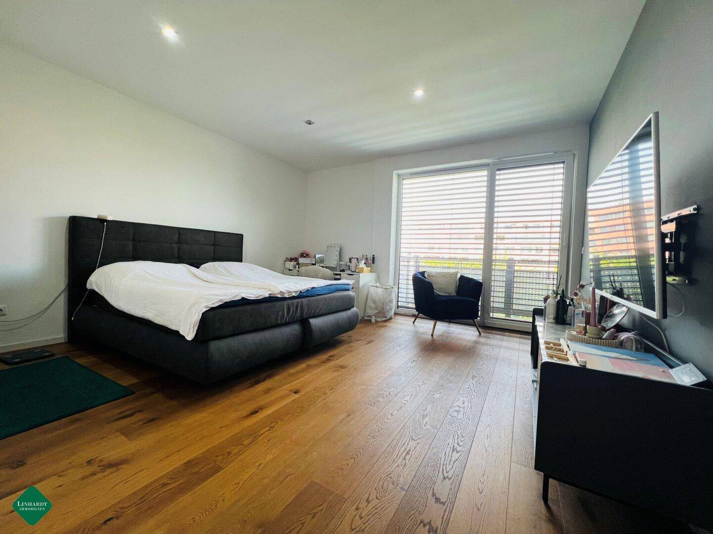 Helles Schlafzimmer mit Holzboden, großem Bett und Zugang zu einem Balkon oder einer Terrasse.