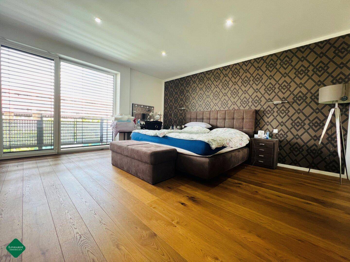 Modernes Schlafzimmer mit Holzboden, gemusterter Akzentwand und viel Tageslicht.