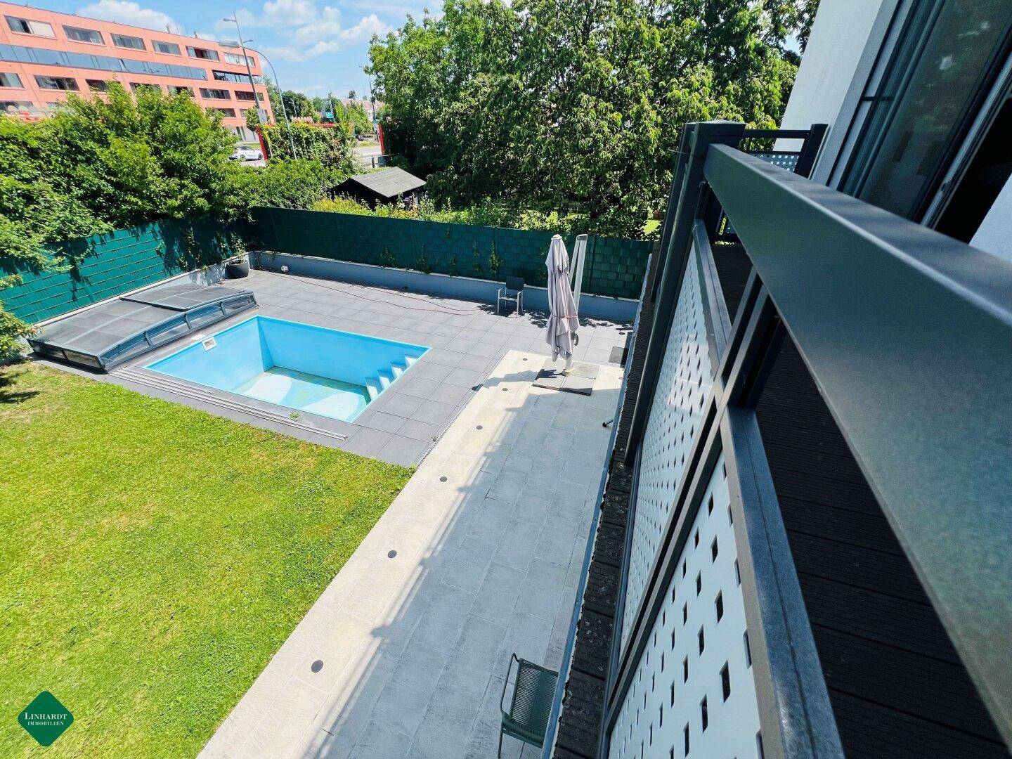 Blick vom Balkon auf den Garten mit Swimmingpool und gepflegter Rasenfläche.
