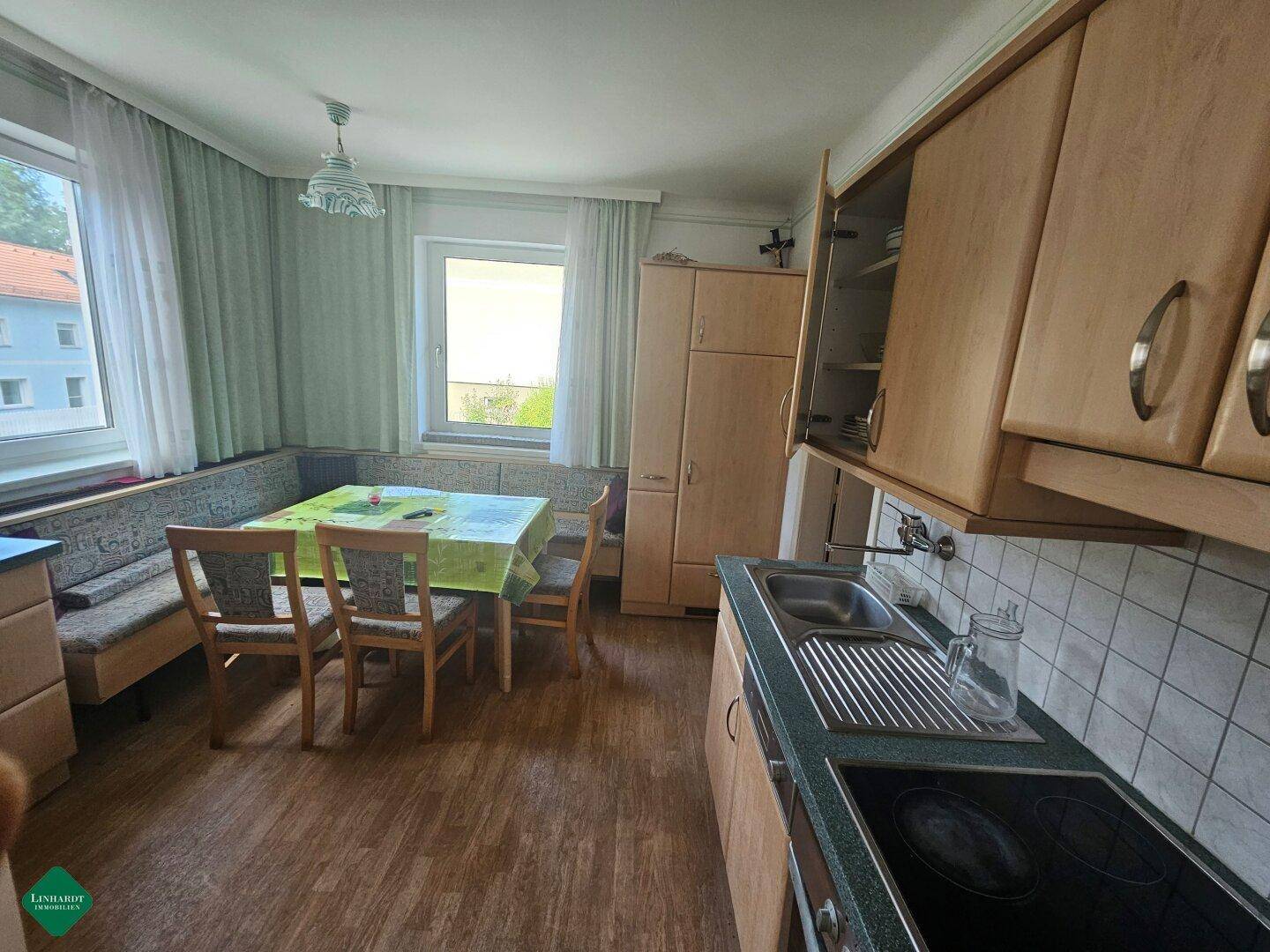 Helle Küche mit Essbereich, Holzschränken, Laminatboden und Blick ins Grüne sowie auf andere Gebäude.