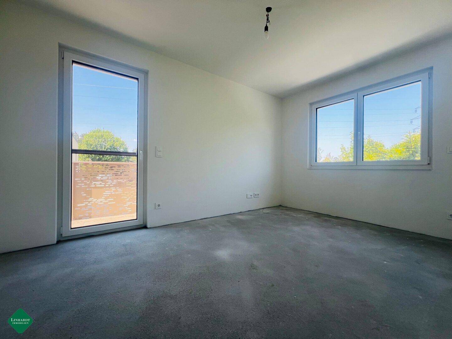 Leeres Schlafzimmer mit viel Tageslicht, Fenster und Zugang zu einem Balkon.