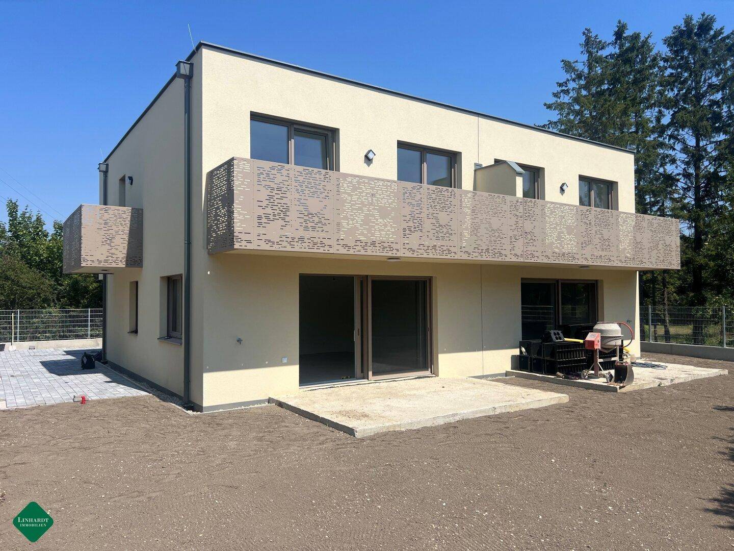 Moderne Neubaufassade mit hellen Wänden und Balkonen, umgeben von unfertigem Gelände.