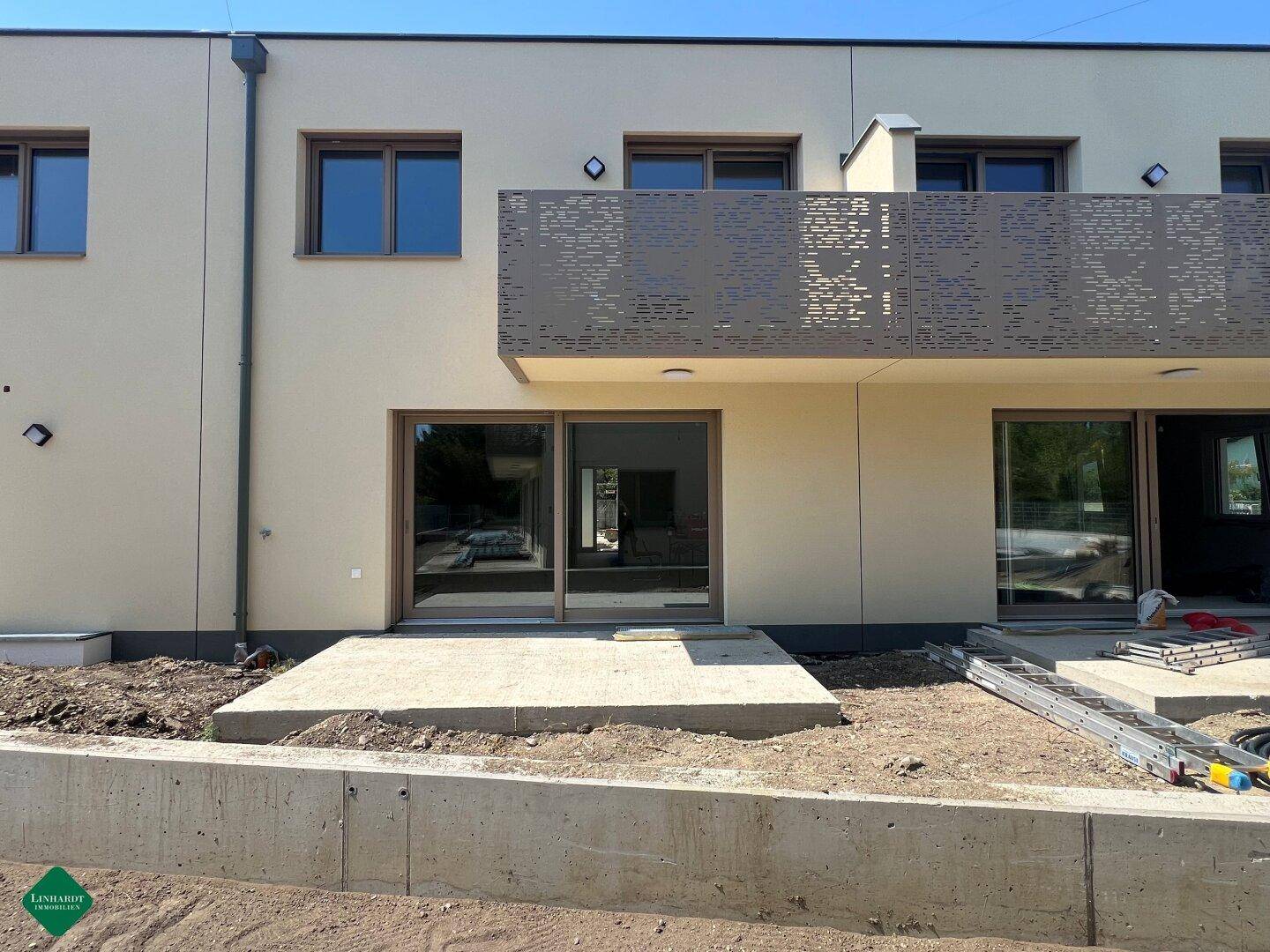 Moderne Gebäudefassade mit großen Glasfronten und einem Balkon, umgeben von unfertigem Gelände.
