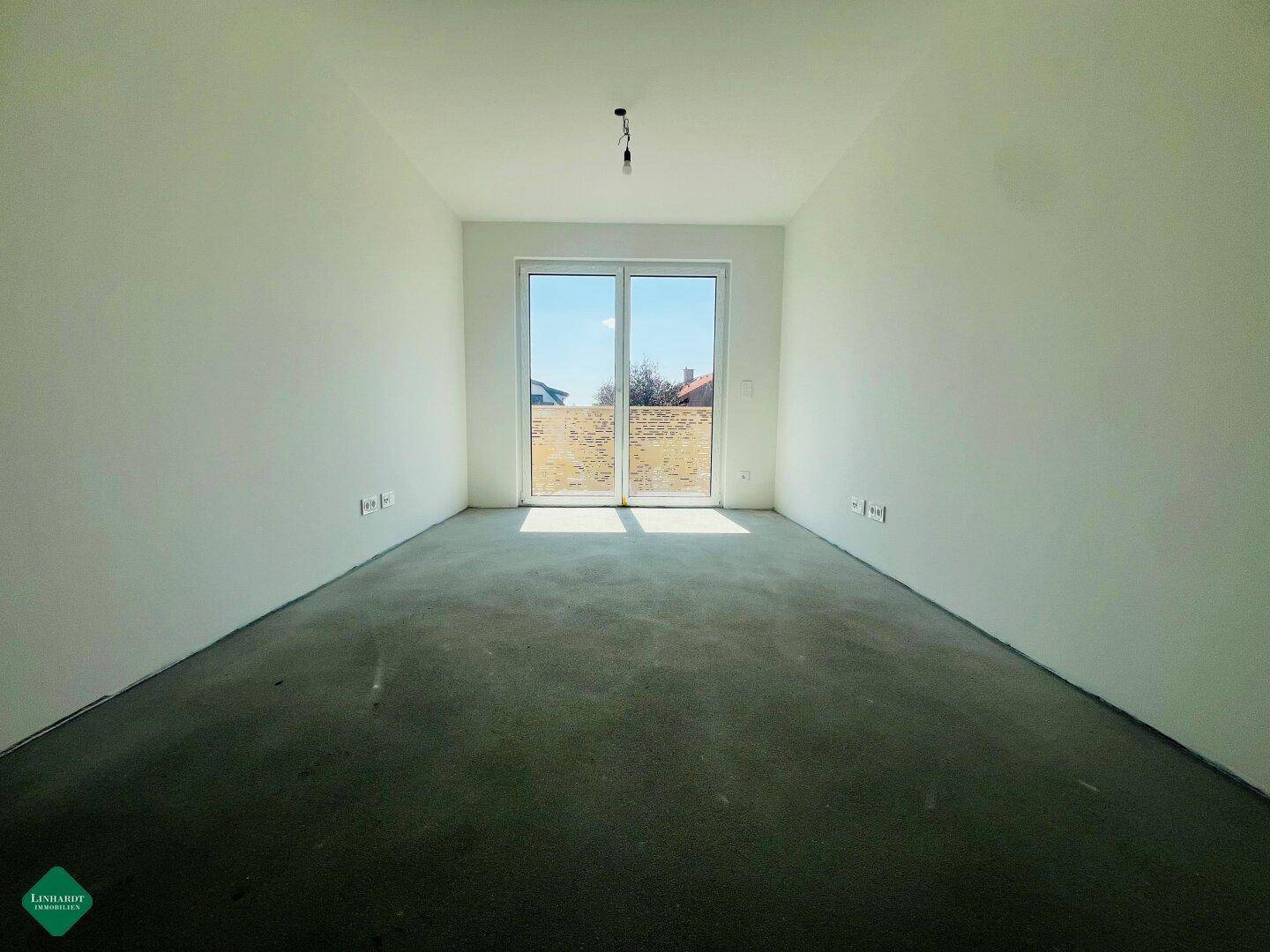 Leeres Zimmer im Neubau mit großen Fenstern, die viel Sonnenlicht hereinlassen.