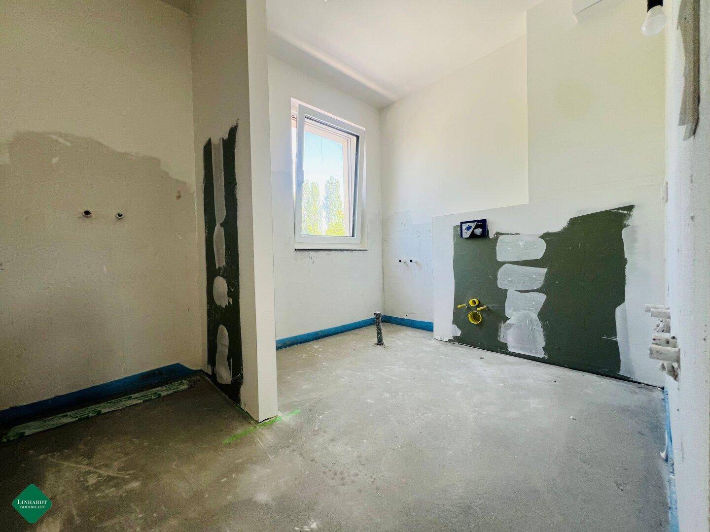 Unfertiges Badezimmer im Neubau mit vorbereiteten Anschlüssen und einem Fenster.