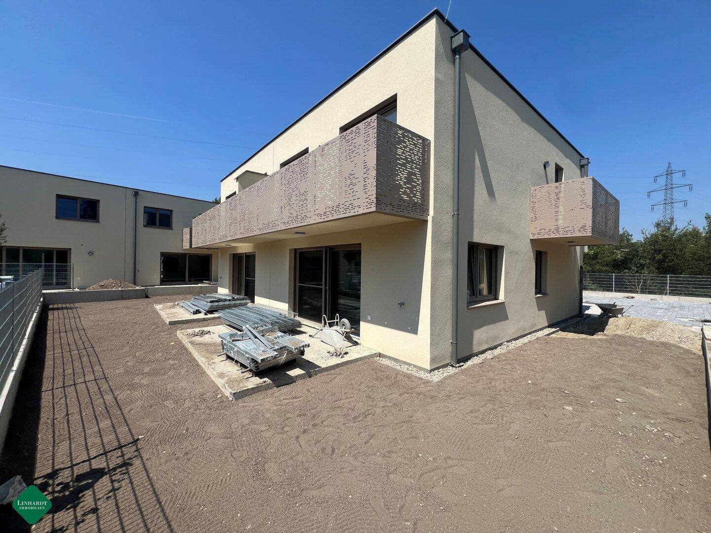 Außenansicht eines neuen Doppelhauses im Bau mit unfertigem Gartenbereich und Balkonen.