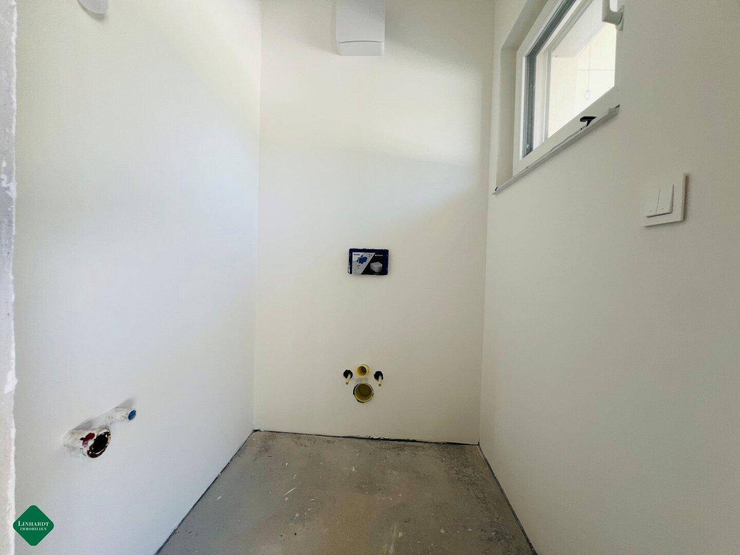 Unfertiges Gäste-WC mit vorbereiteten Anschlüssen für Toilette und Waschbecken sowie einem Fenster.