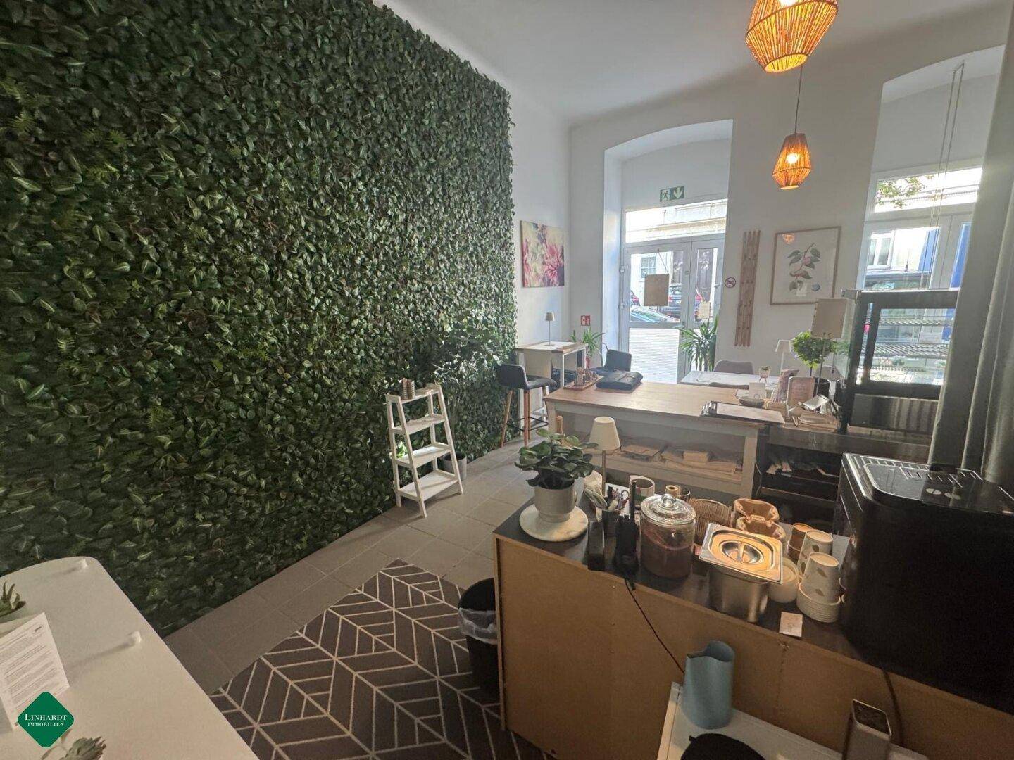 Heller Innenraum eines Cafés mit einer auffälligen grünen Wand, Holztischen und großen Fenstern zur Straße.