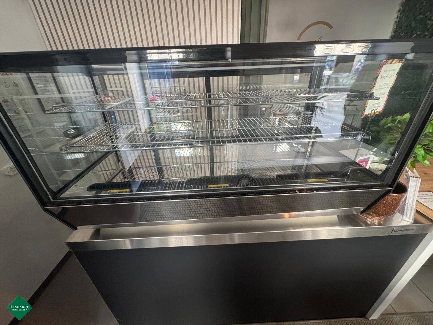 Nahaufnahme einer modernen, schwarzen Kühlvitrine mit Glasfront und Edelstahlregalen für Lebensmittelpräsentation.