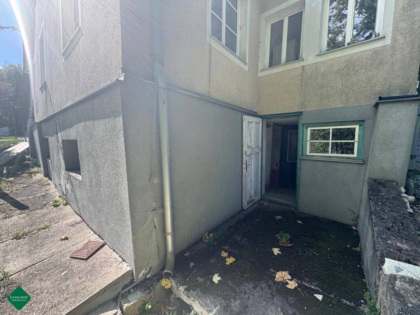 Eingangsbereich zum Untergeschoss des Hauses mit alter Holztür und Betonplatten.