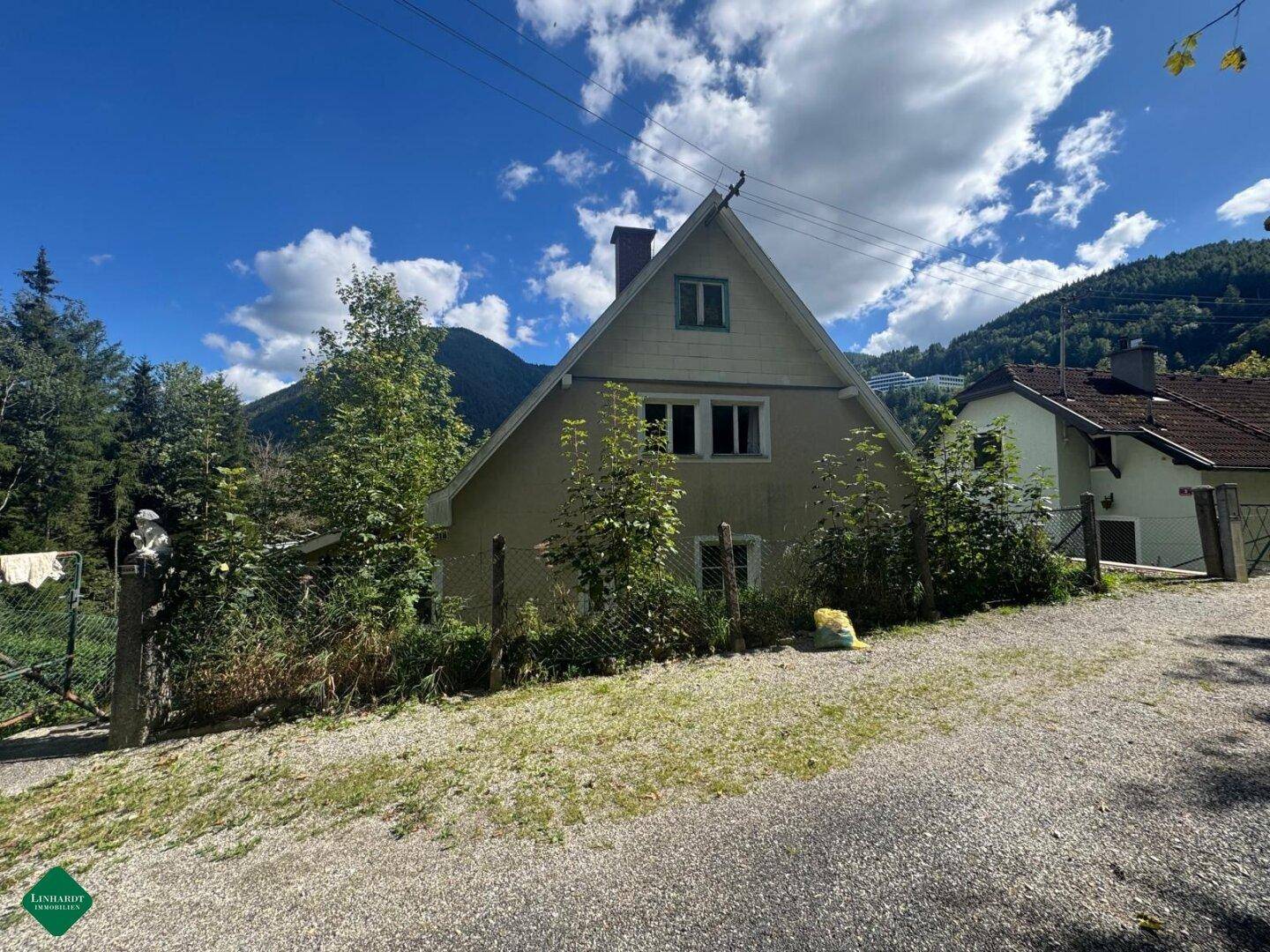 Seitenansicht des Hauses mit Schrägdach, umgeben von Bäumen und Blick auf die Berge.