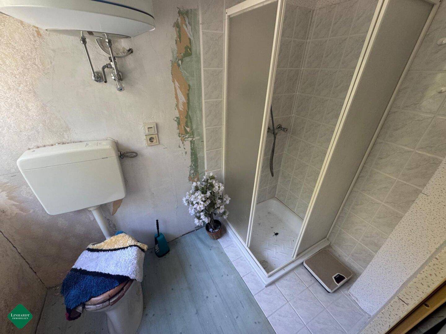 Badezimmer mit Dusche, Toilette und Boiler, in sanierungsbedürftigem Zustand.