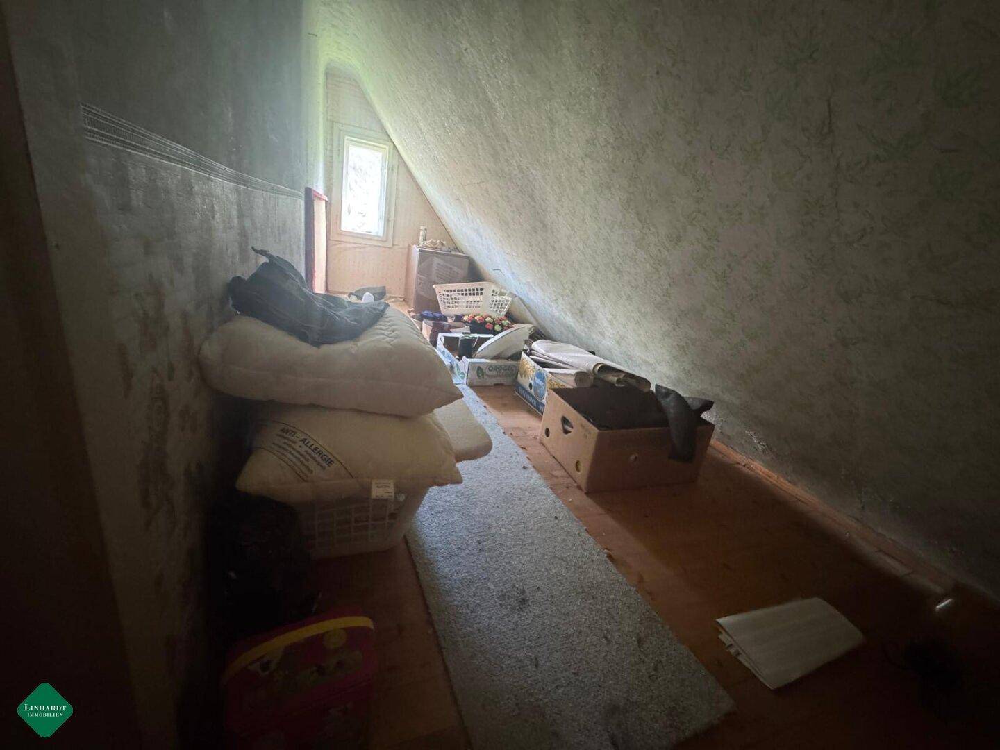 Dachboden als Abstellraum genutzt mit schrägen Wänden und kleinem Fenster.