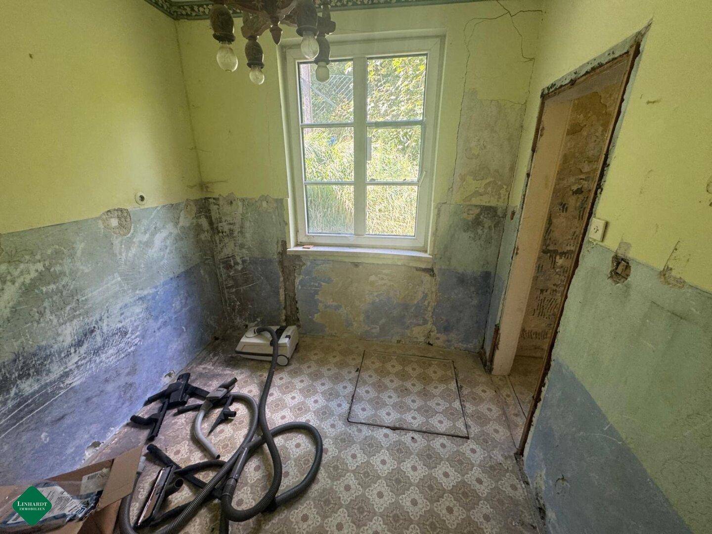 Leerer Raum mit alten Tapetenresten, Fenster und Fliesenboden, bereit zur Sanierung.