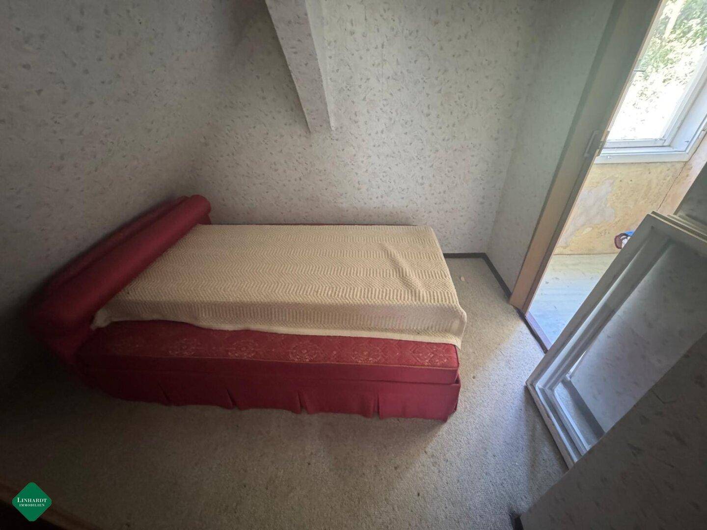Schlafzimmer im Dachgeschoss mit Bett, Teppichboden und schrägen Wänden, renovierungsbedürftig.