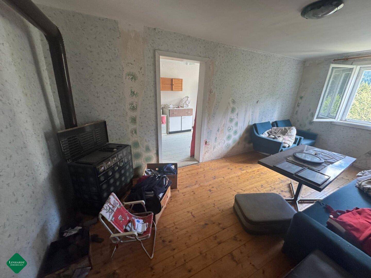 Wohnzimmer mit Holzofen, Holzboden und Tapetenresten, bereit für eine Renovierung.