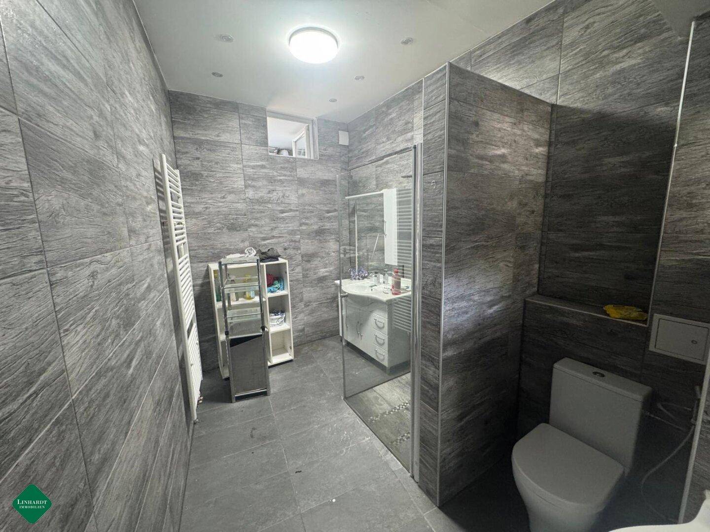 Modernes Badezimmer mit dunkelgrauen Fliesen, begehbarer Dusche und beheiztem Handtuchhalter.