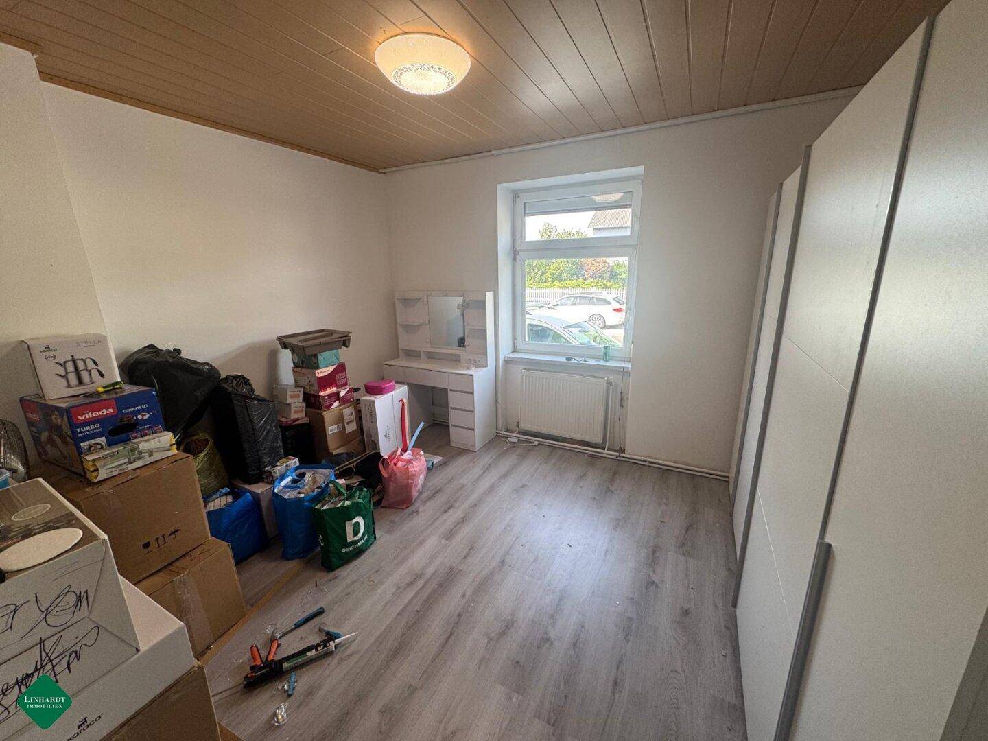 Zimmer mit Laminatboden, Fenster und einem Schminktisch, derzeit als Abstellraum genutzt.