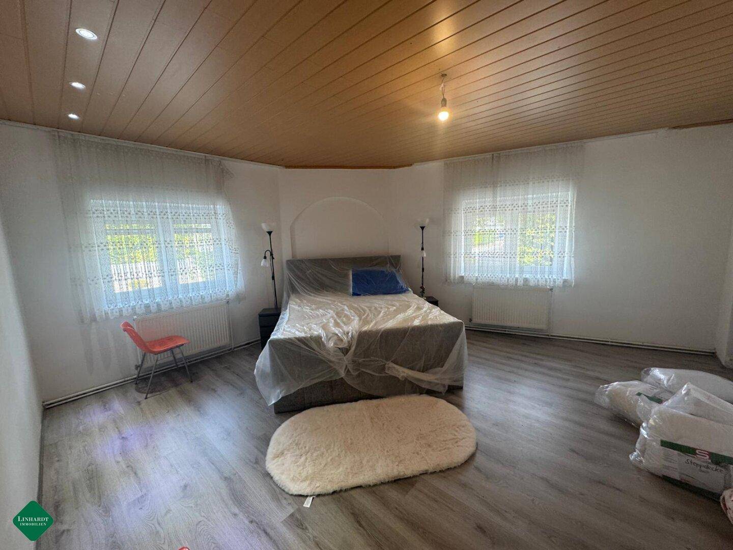Helles Schlafzimmer mit Holzlattendecke, Laminatboden und zwei Fenstern.