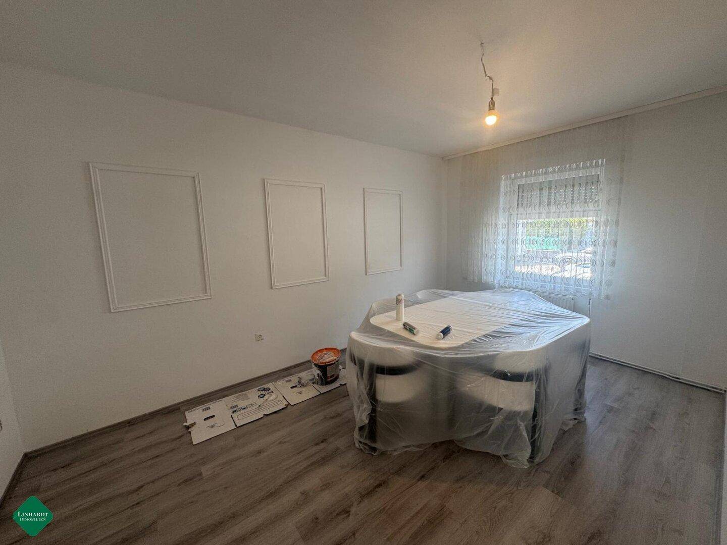 Essbereich mit Laminatboden, weiß gestrichenen Wänden und einem Fenster mit Vorhängen.