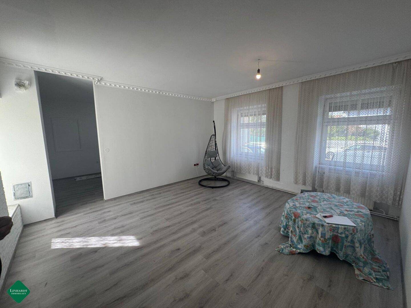 Geräumiges Wohnzimmer mit Laminatboden, Zierleisten an der Decke und viel Tageslicht.