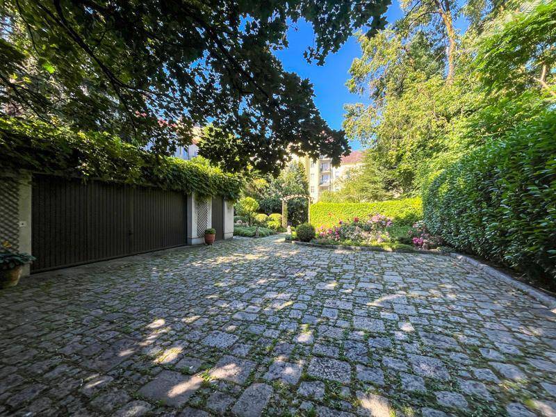 Geräumiger gepflasterter Innenhof mit Garagentoren, umgeben von üppigem Grün und Bäumen.