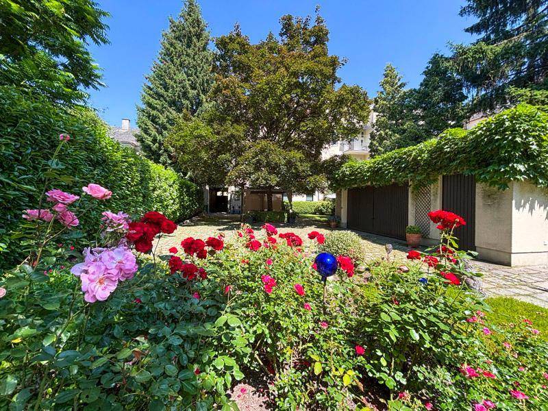 Farbenfroher Rosengarten mit blühenden Blumen und einem gepflasterten Weg, umgeben von Bäumen.