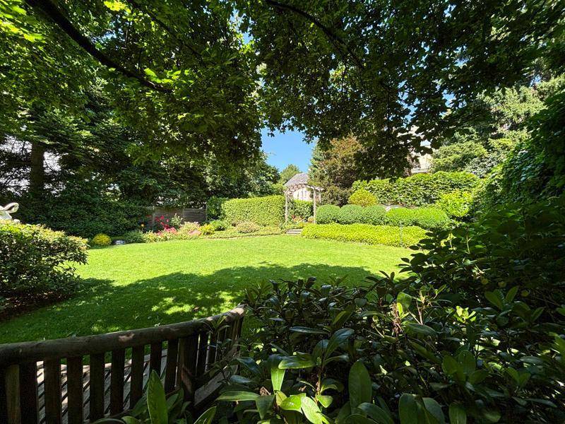 Weitläufiger, gepflegter Garten mit Rasenfläche, Hecken und einem kleinen Pavillon im Hintergrund.
