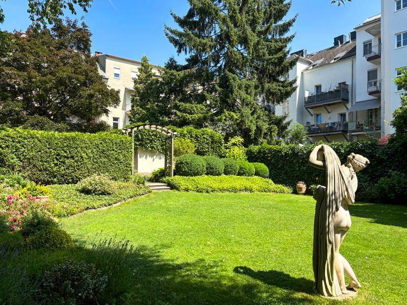 Großer, sonniger Garten mit Rasen, Hecken und einer klassischen Statue als Dekoration.