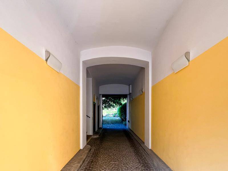 Heller Durchgangsbereich mit gelben Wänden und einem gepflasterten Boden, der ins Grüne führt.