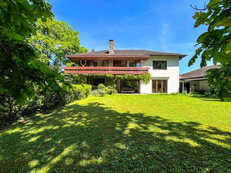 Eindrucksvolles Einfamilienhaus mit weißer Fassade und Holzbalkonen, umgeben von einem großen Garten.