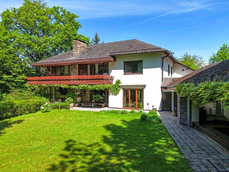 Großzügiges Einfamilienhaus mit weißer Fassade, Holzelementen und weitläufigem Gartenbereich.