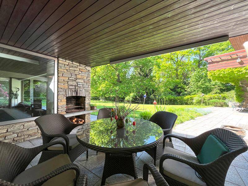 Überdachte Terrasse mit Essbereich, Steinkamin und Blick auf den weitläufigen Garten.