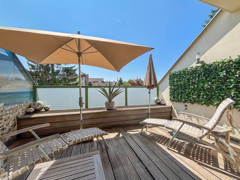 Sonnige Dachterrasse mit Holzdeck, Liegestühlen und einem großen Sonnenschirm.