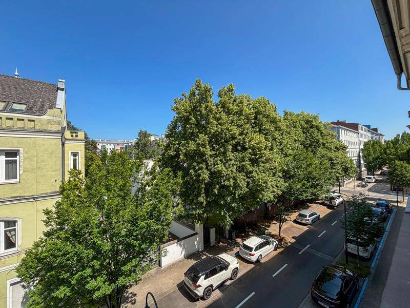 Blick von oben auf eine ruhige Wohnstraße mit parkenden Autos und vielen Bäumen.
