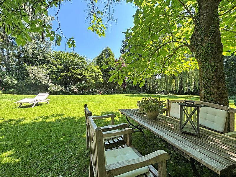 Idyllischer Gartenbereich mit Holztisch und Bänken unter einem schattenspendenden Baum an einem sonnigen Tag.