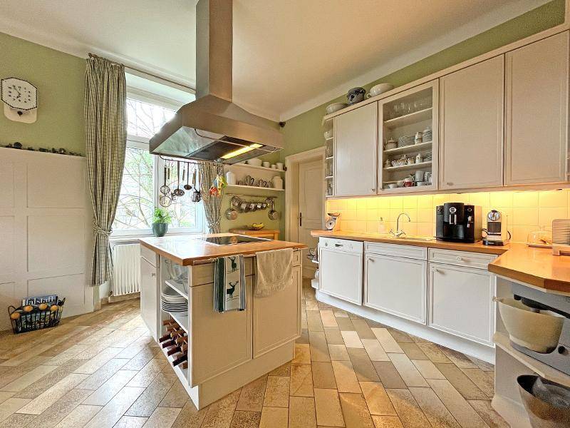 Helle Küche mit Kücheninsel, weißen Schränken, Holztheke und traditionellem Fliesenboden.